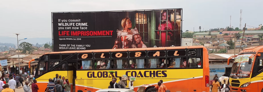 A bus passes by a billboard showcasing WildAid's campaign about how wildlife crime can result in lifetime imprisonment. The billboard depicts a man behind bars looking out at his wife and three children.