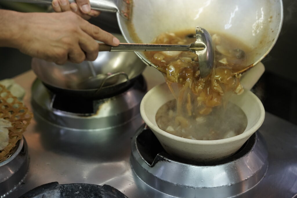 A bowl of shark fin soup is poured from a pan into a warmer.